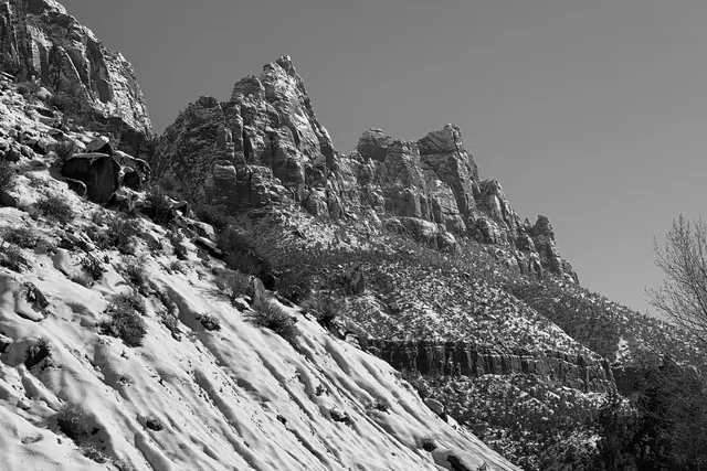A steep snowy slope below a craggy peak, in black and white