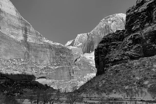 A sunlit sandstone cliff beside a shadowed snowy canyon, in black and white