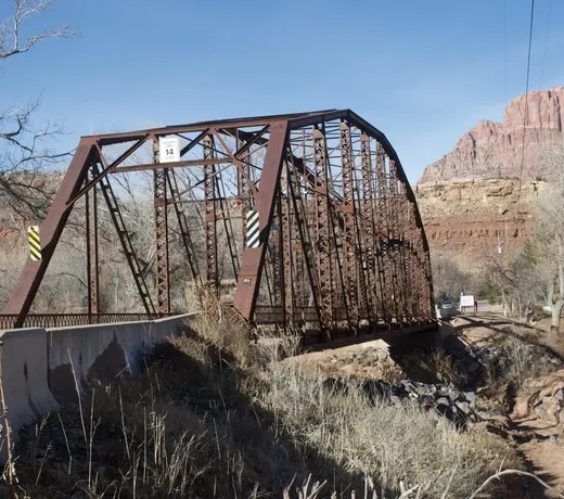 Historic one-lane iron truss bridge over the Virgin River in Rockville Utah, with Zion cliffs behind