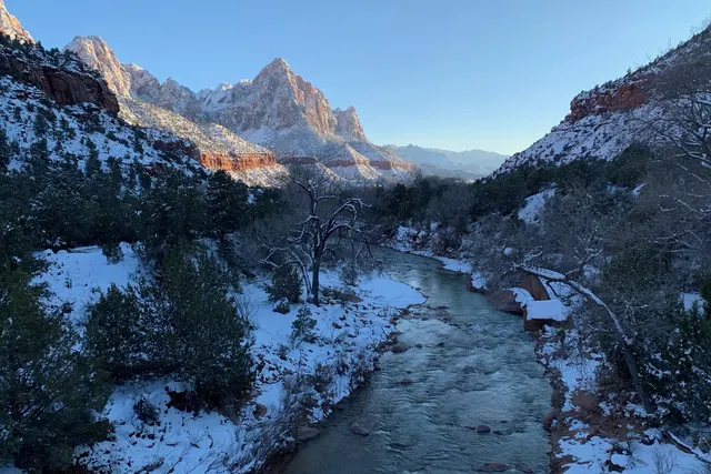 A river running between snowy banks below a jagged red and white peak