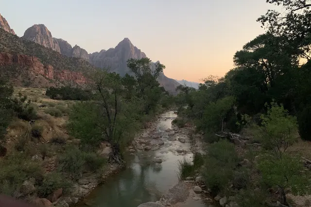 A rocky river below a pointed peak under a soft pink and peach sky