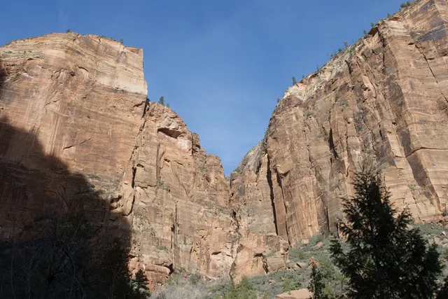 Sunlit red sandstone cliffs narrowing into a canyon under a gray-blue sky