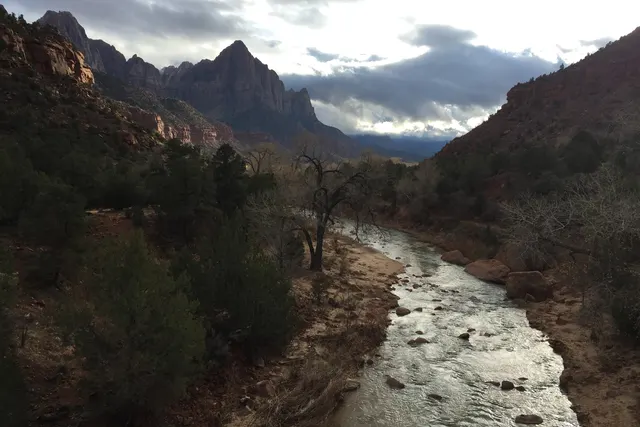 A river flowing below dark canyon walls toward a distant peak under scattered cloud