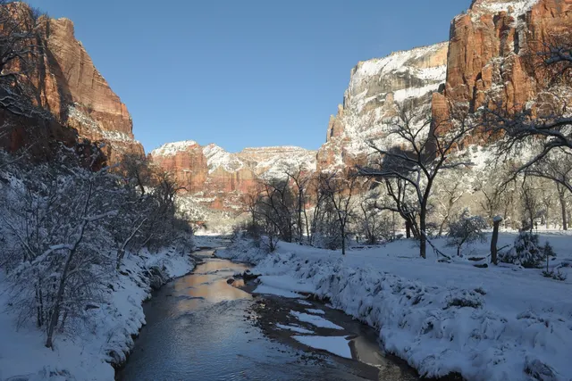 A narrow river channel between snowy banks below tall red cliffs