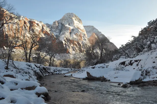 Snow along a river bank with snow-covered peaks rising behind