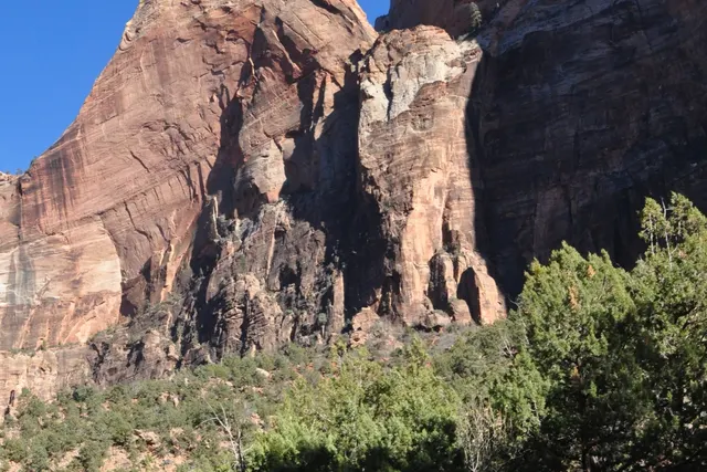 A red sandstone buttress rising above green shrubs under a blue sky