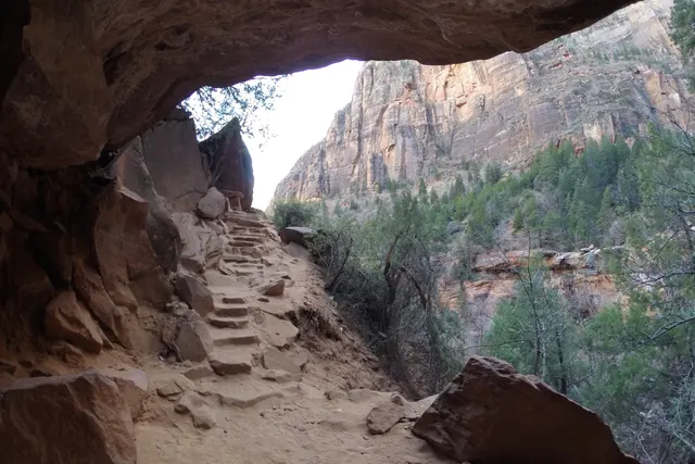 A carved sandstone alcove with stone steps and a view of a pale canyon wall beyond