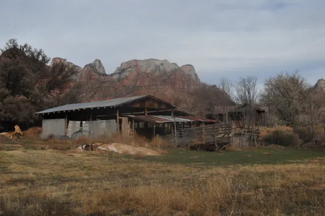 A weathered wooden barn with red rock hills behind it under an overcast winter sky