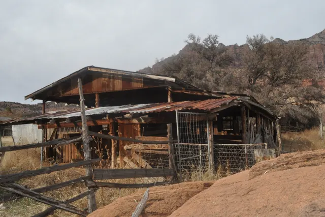 A close view of a rusty-roofed wooden barn and wire fencing
