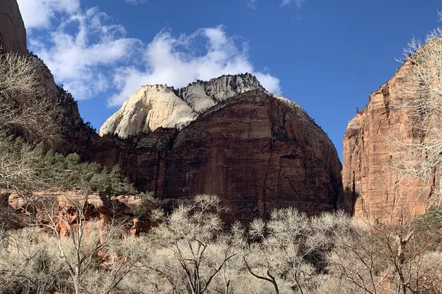 A domed red and white sandstone cliff under blue sky and clouds