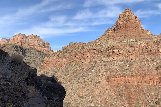 A sandstone peak seen across a canyon under a blue and white sky