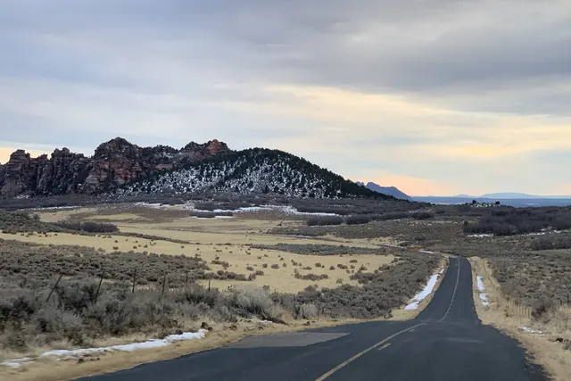 A road running through open country toward snow-dusted red hills