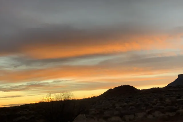 Bands of orange and teal light across a dark hill silhouetted at dusk