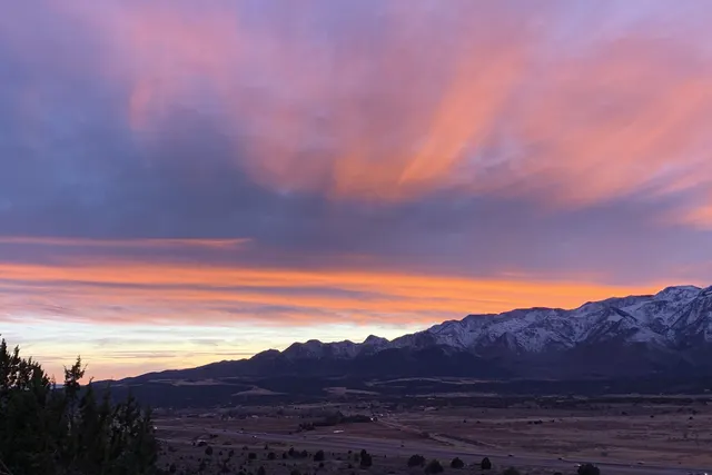 Pink and violet clouds streaking over a dark mountain range with pale snow on its crest