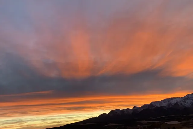 Fiery orange clouds fanning across a purple sky above a low dark ridgeline